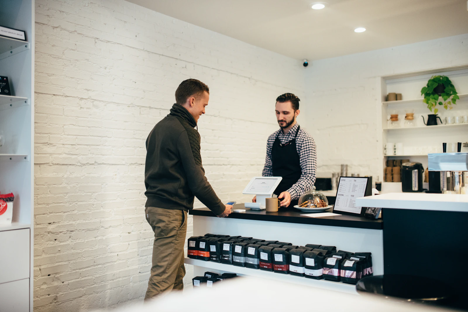 A customer paying at a coffee shop counter while the owner rings up the sale
