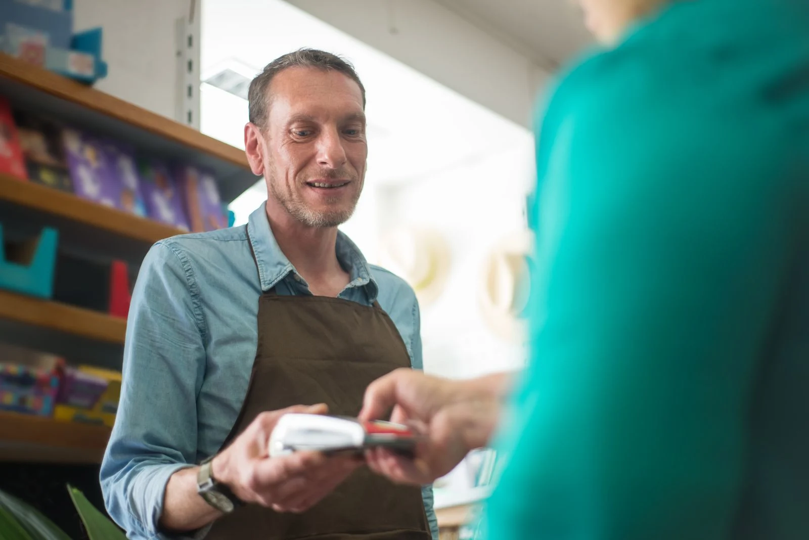 A shopkeeper handing a card terminal to a customer across the counter
