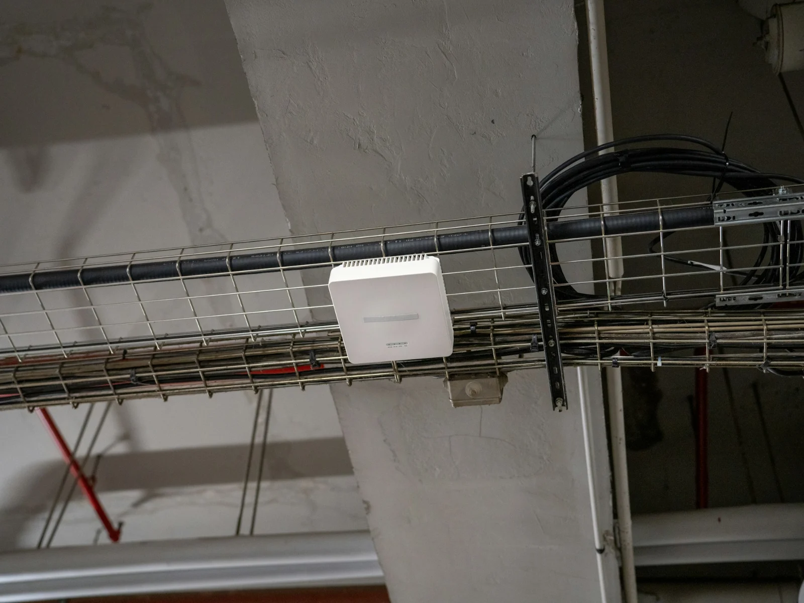 A white Wi-Fi access point mounted on a cable tray under an office ceiling