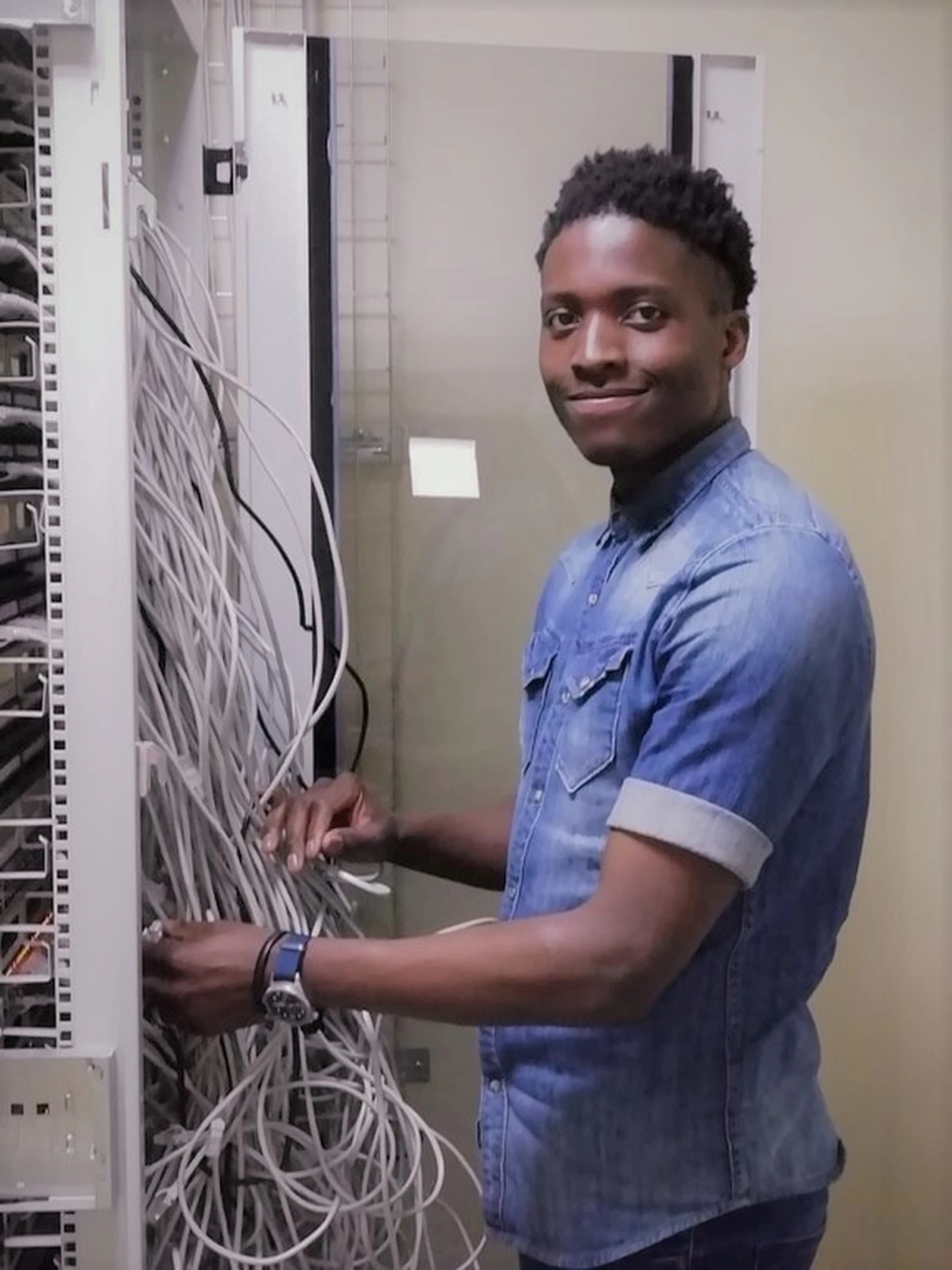 An IT technician smiling beside the phone and network cabinet he is wiring
